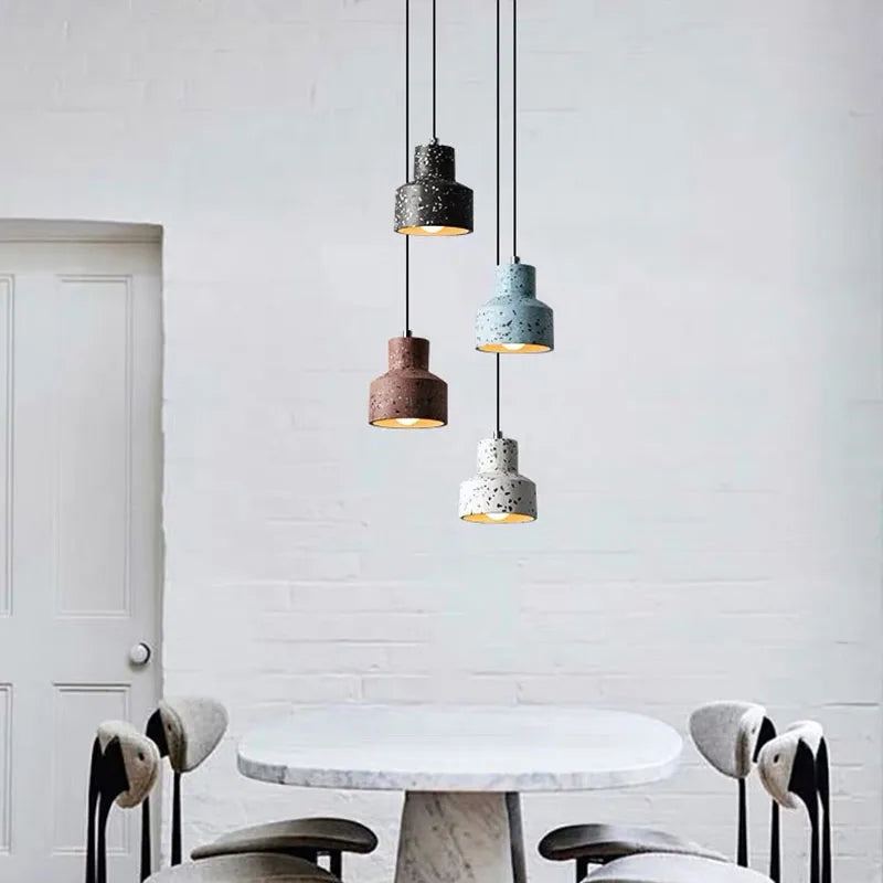 LUXELY terrazzo cement pendant lights in assorted colors, suspended above a round table in a minimalist white interior setting.