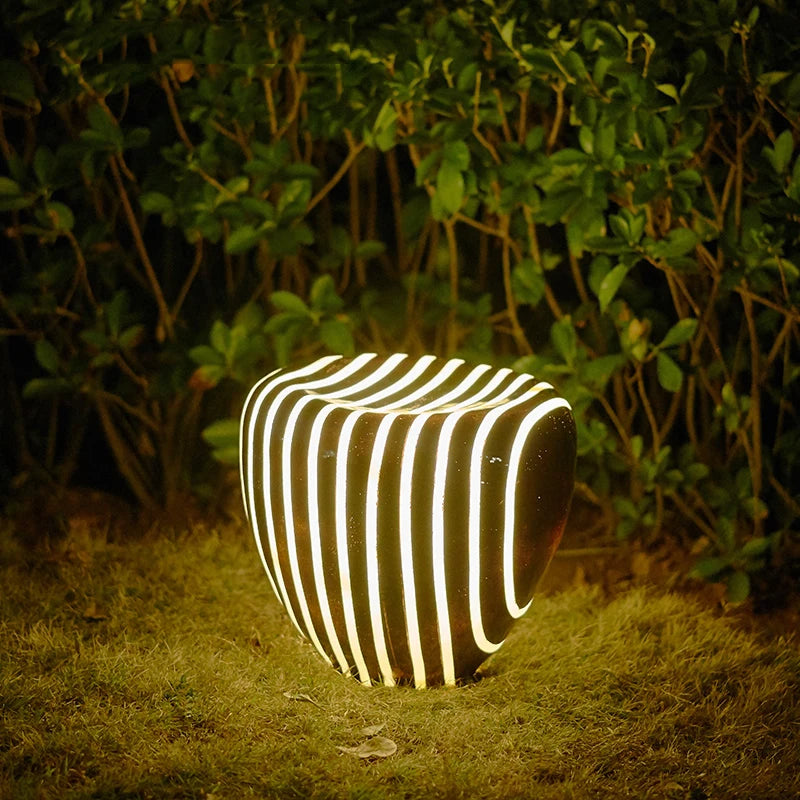 Waterproof stone garden light illuminating a grassy area, perfect for outdoor pathways and patios with modern striped design.