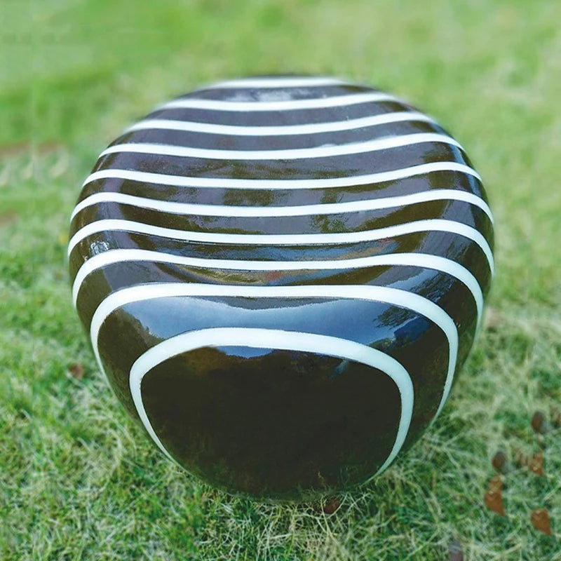 LUXELY stone garden light with black and white striped design shown unlit on grass, highlighting its sculptural modern form.