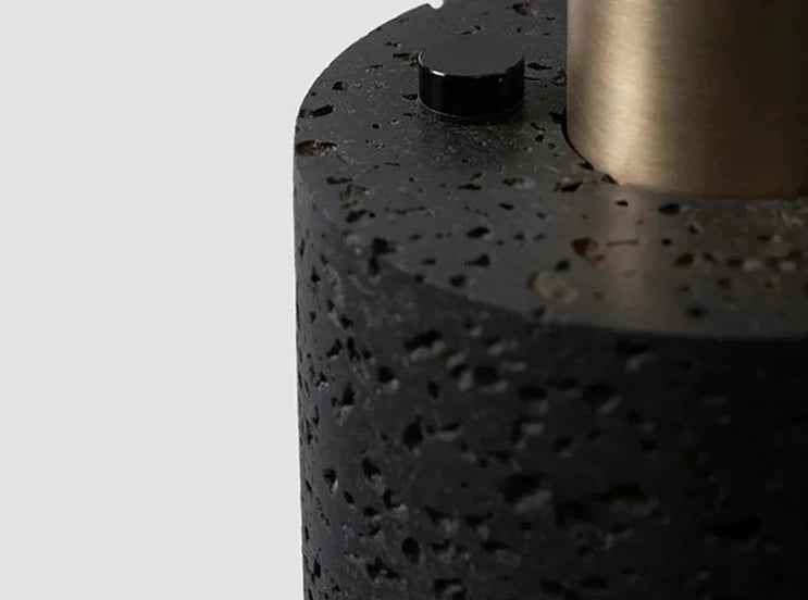 Close-up of LUXELY terrazzo pendant light showing textured black cement and brass detail. High-end industrial lighting finish.