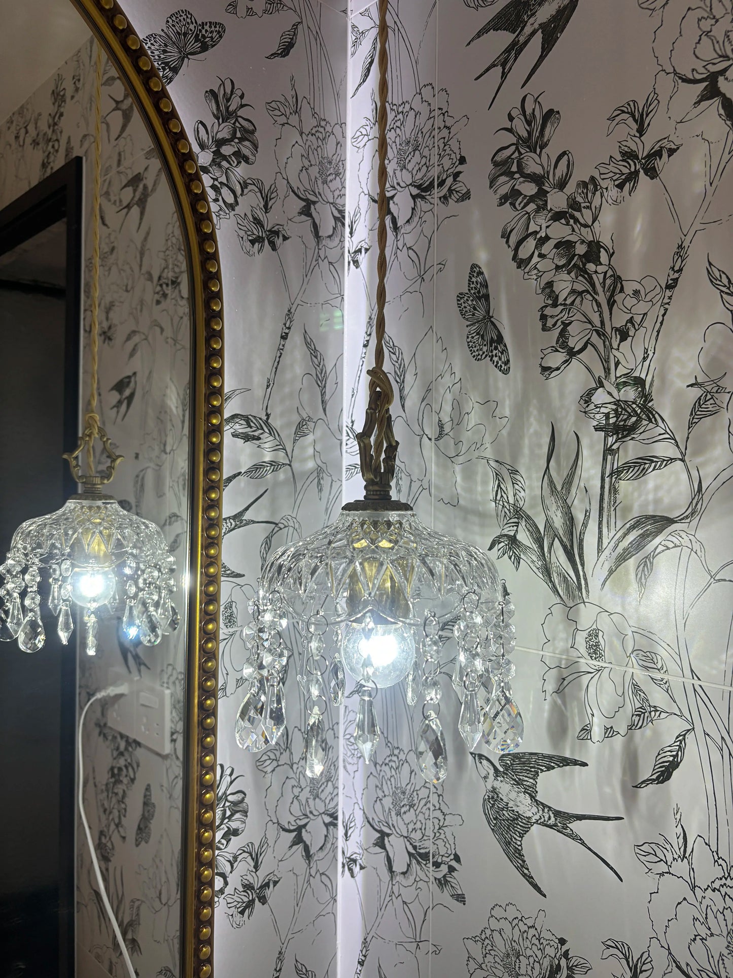 French Vintage Crystal Chandelier - Copper Hanging Lamp with LED bulb, reflecting light on floral wallpaper and mirror.