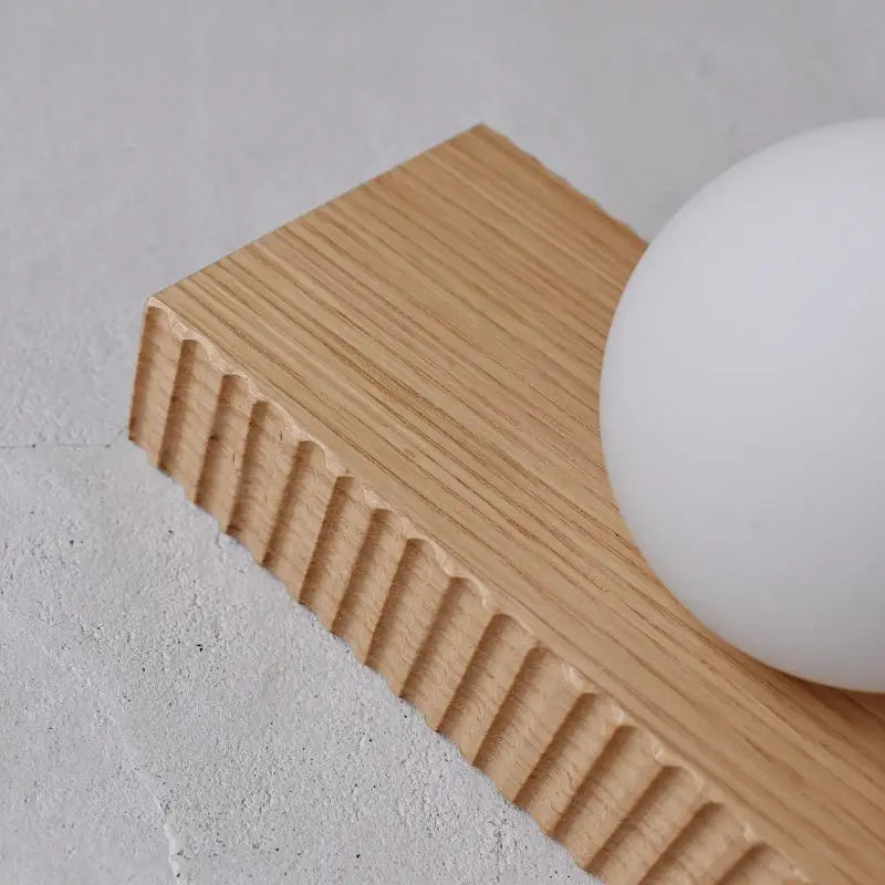 Close-up of light oak wood texture and frosted globe on the LUXELY wall lamp, ideal for modern bedroom lighting.