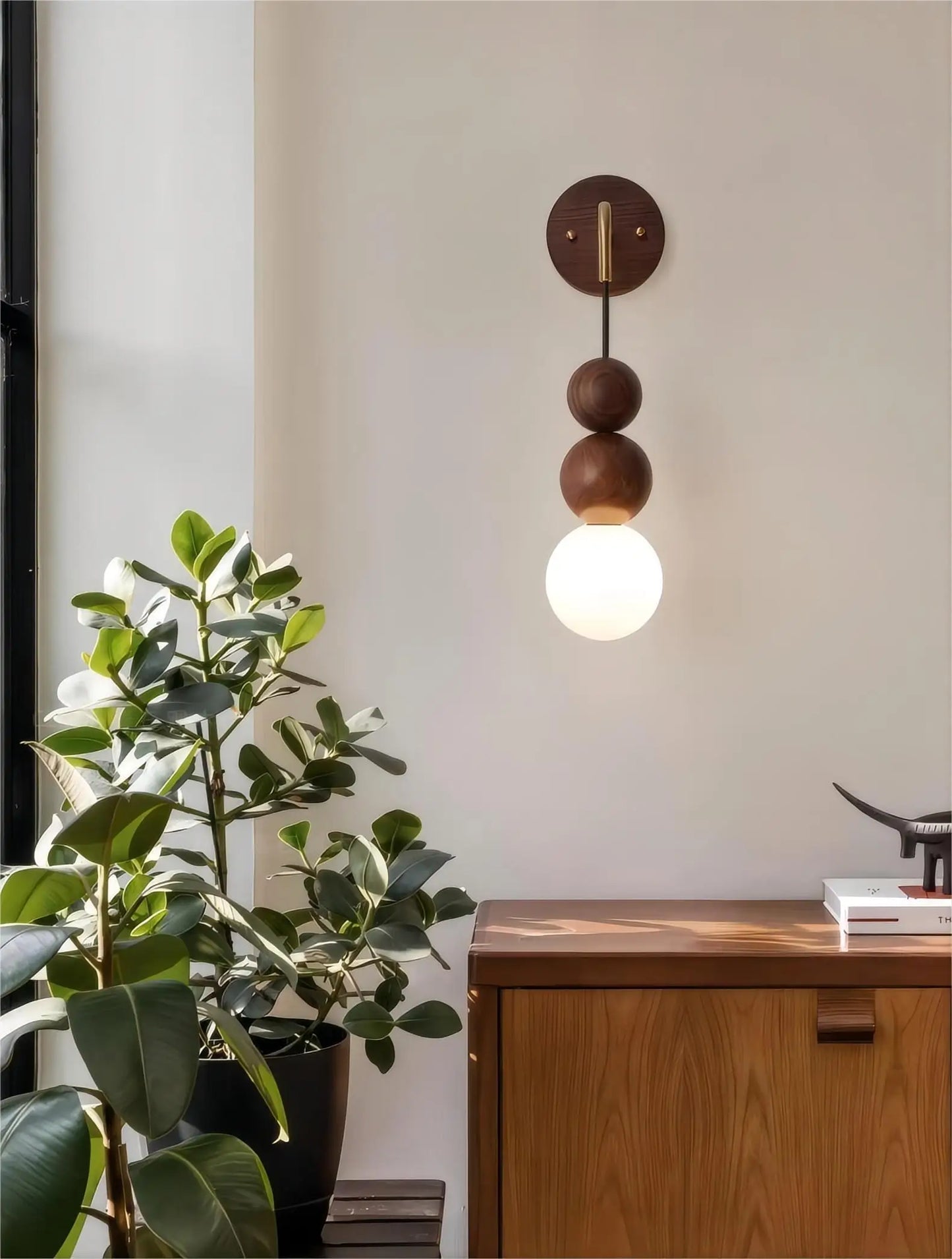 LUXELY walnut wood and brass wall sconce with glowing globe, styled above wooden cabinet in a modern interior.