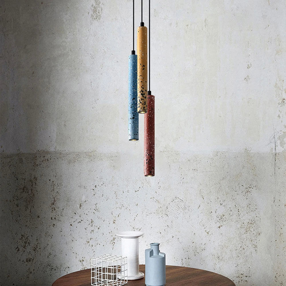 Three LUXELY industrial pendant lights in red, blue, and yellow tones over a round table. Sleek LED design for modern home lighting.