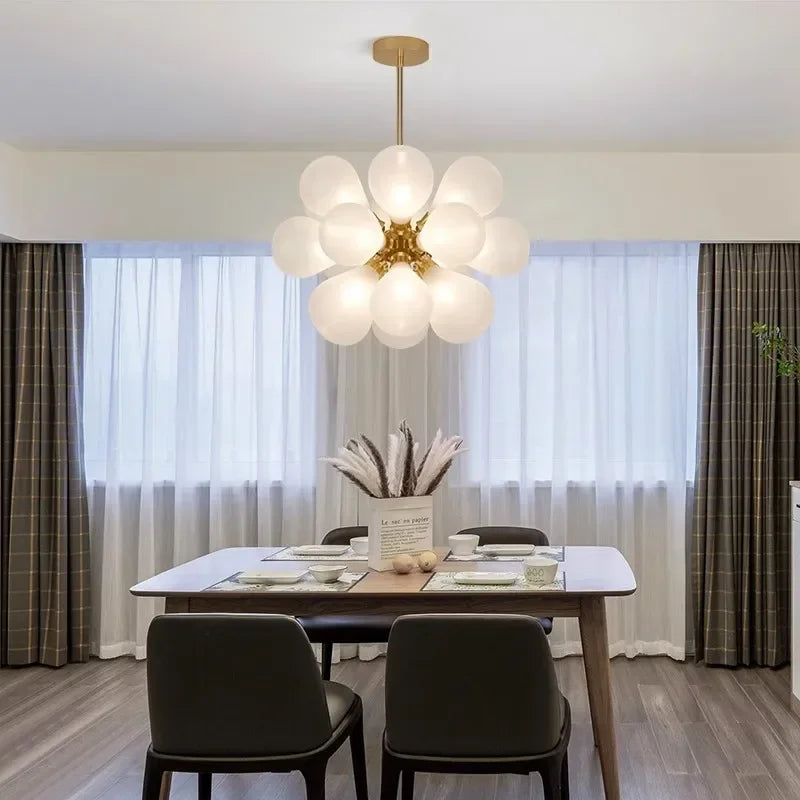 White bubble glass Scandinavian chandelier with gold accents, suspended above a dining table for a soft, modern glow.