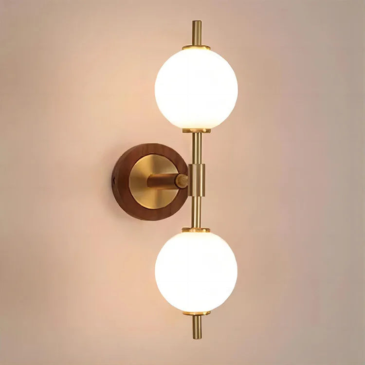 Brass and wood wall light with vertical globe design, casting warm light on a neutral wall for modern interiors.
