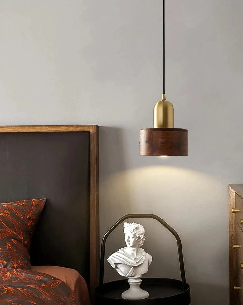 Stylish LUXELY pendant light in walnut and brass hanging beside a bed, ideal for bedroom or hotel lighting design.