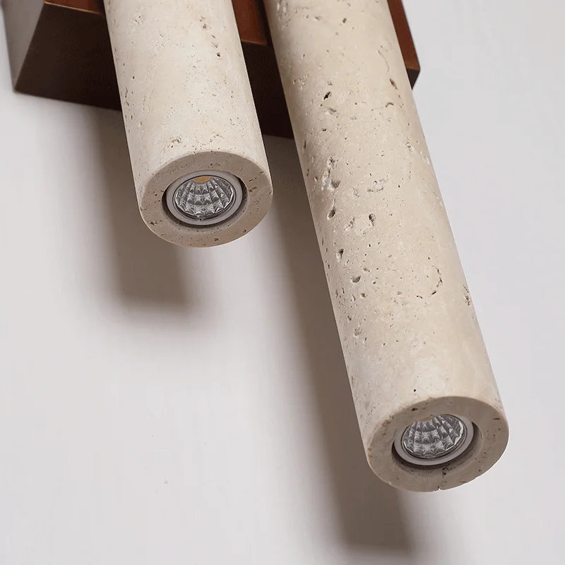 Close-up of travertine stone wall lamp showing LED light source embedded in cylindrical stone tubes with wood base.