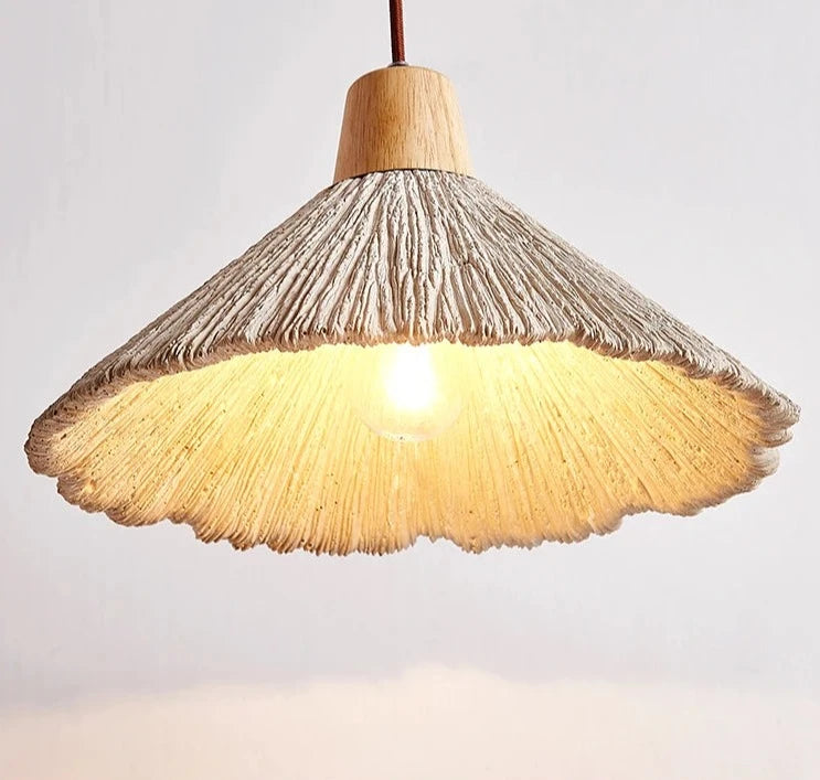 Warmly lit travertine pendant lamp with exposed bulb, highlighting natural texture and scalloped edge for cozy interior lighting.