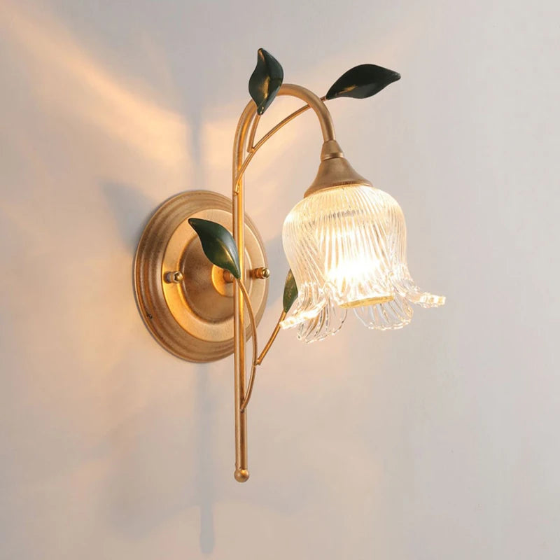 French Wall Sconce Light with golden branch and green leaf design, featuring a fluted glass flower shade and LED bulb for bedroom lighting.