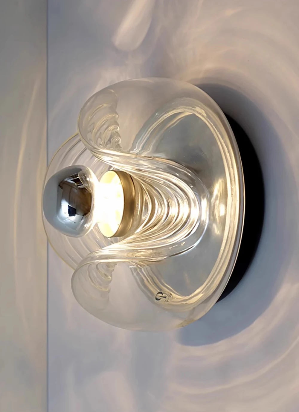 Angled view of designer glass wall sconce with LED light, featuring artistic curves and warm illumination.