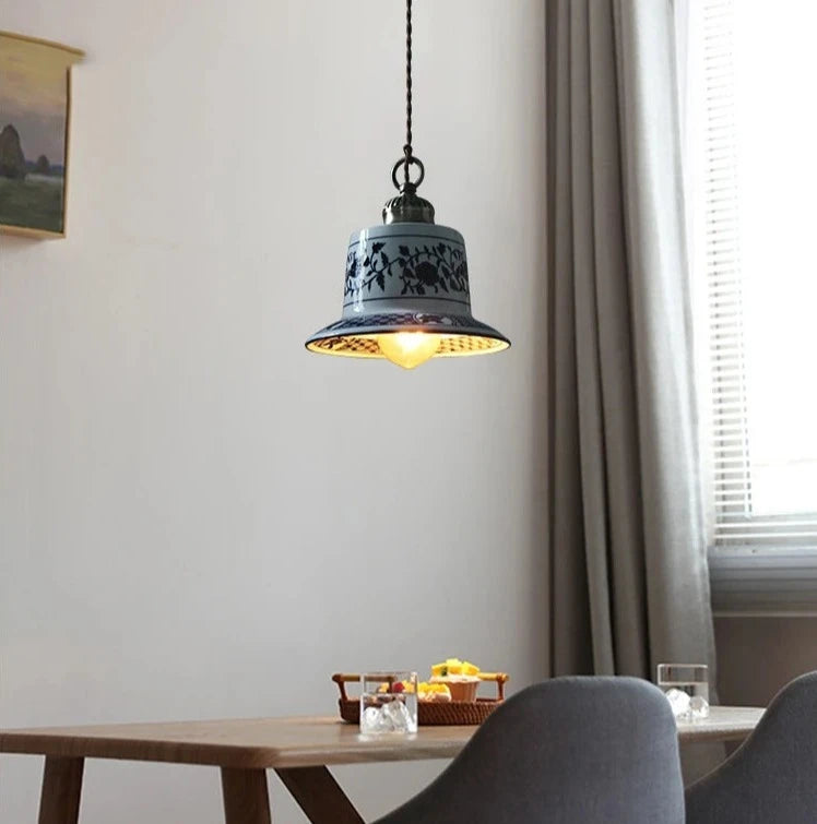 Bell-shaped ceramic pendant light with blue floral pattern, casting warm LED light over a dining table.