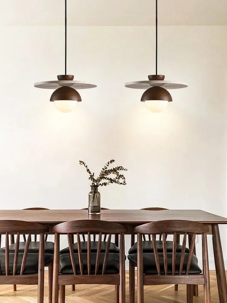 Pair of walnut wood and stone pendant lights over dining table, minimalist LED fixtures for contemporary dining rooms.
