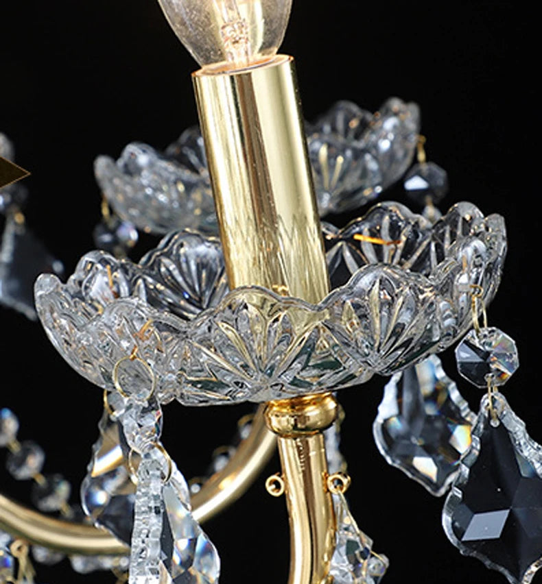 Close-up of candle-style light holder on golden crystal chandelier with faceted crystal dish and gold trim.