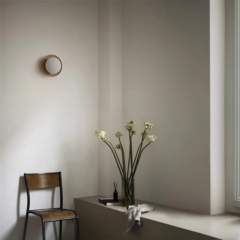 Brass accent wall sconce with light wood finish, installed in minimalist reading nook with natural decor.