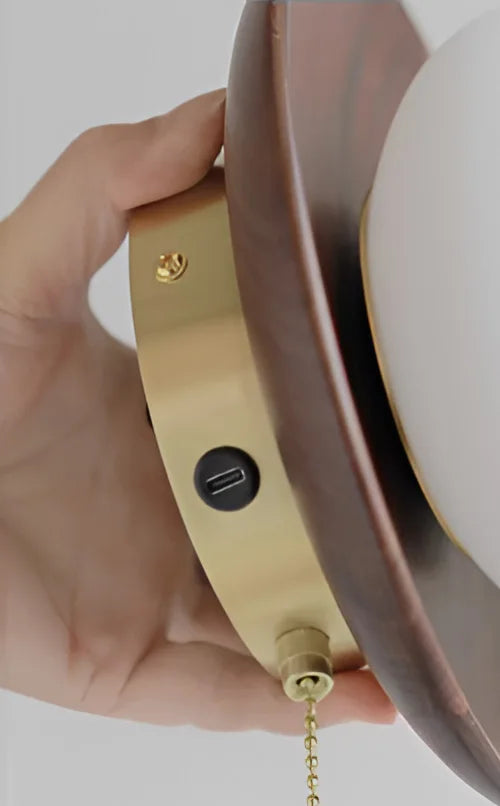 Close-up of brass base with USB port and pull chain on walnut wood wall lamp, showcasing smart lighting features.