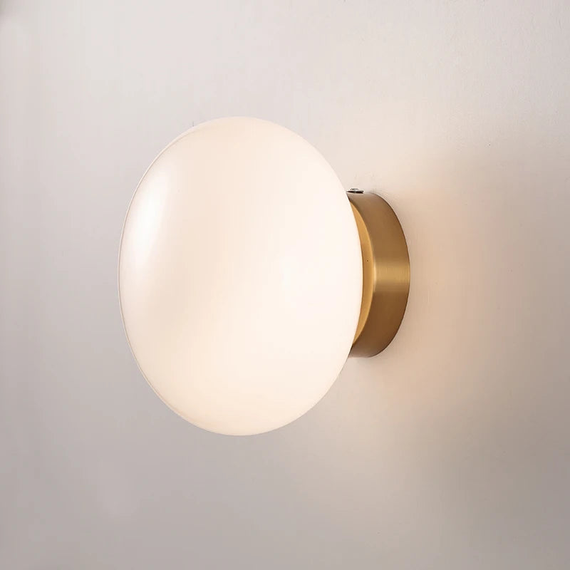 Close-up of LUXELY modern wall light with brass base and opal glass shade, highlighting its elegant finish and soft LED glow.