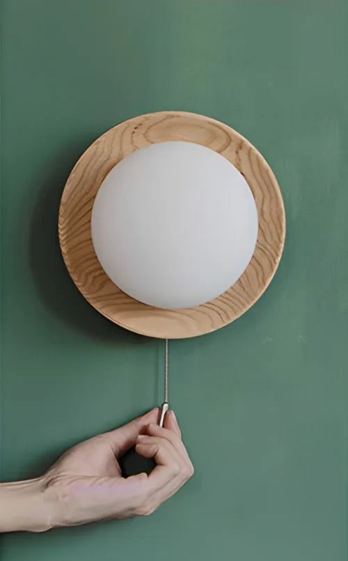 Pull-chain operated light wood wall sconce with frosted globe, combining functionality with Nordic design.