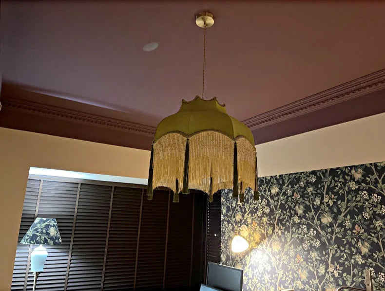Green velvet tassel chandelier with soft lighting, suspended from a purple ceiling in a floral-themed room.