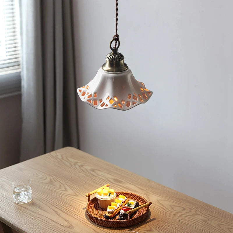 LUXELY ceramic pendant light with decorative cut-out design, casting warm LED light over a wooden dining table.