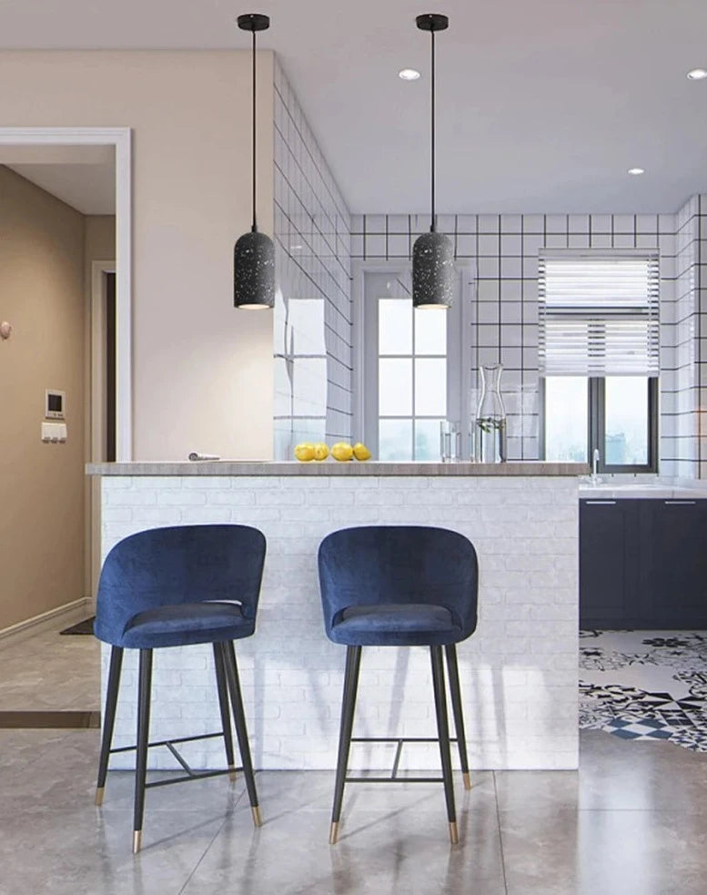 Pair of dark terrazzo LUXELY pendant lamps above a kitchen bar with blue stools. Industrial cement lighting for modern kitchens.