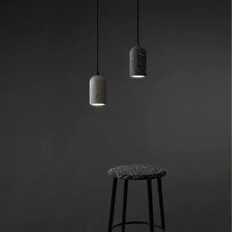 Two LUXELY terrazzo cement pendant lights hanging over a modern black stool. Perfect for minimalist bar or coffee shop decor.