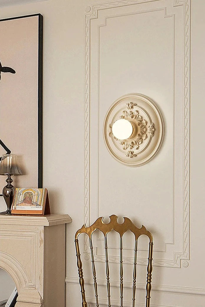 Beige LUXELY wall sconce with ornate design, mounted in a vintage-style room above a gold chair for ambient lighting.