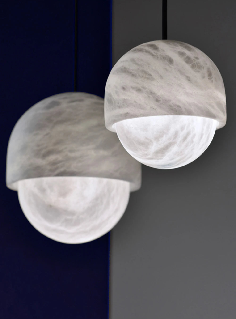 Close-up of two dome-shaped marble LED pendant lights. Marble LED pendant light – modern ceiling lamp dimmable for soft interior lighting.