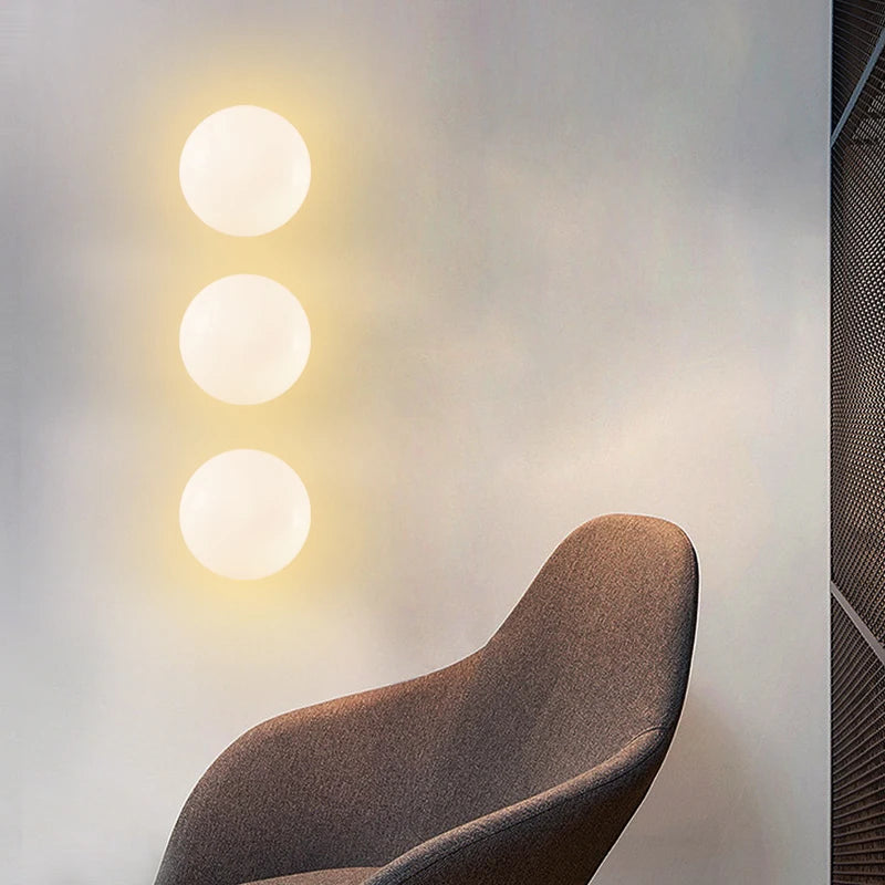 Three LUXELY modern brass wall lights installed vertically, providing warm ambient lighting in a contemporary seating area.