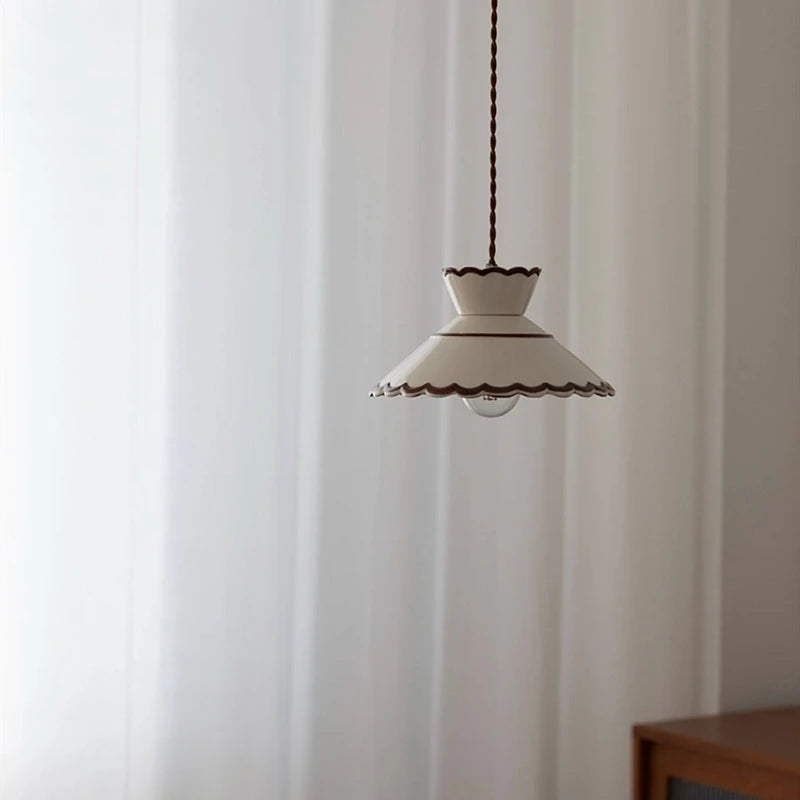 Vintage ceramic pendant lamp with scalloped trim and LED bulb, suspended in a softly lit modern interior.