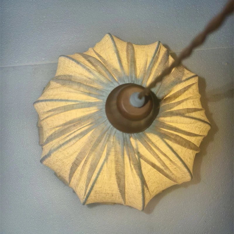 Illuminated Japanese fabric pendant lamp viewed from below, showing warm light diffusion through pleated fabric.