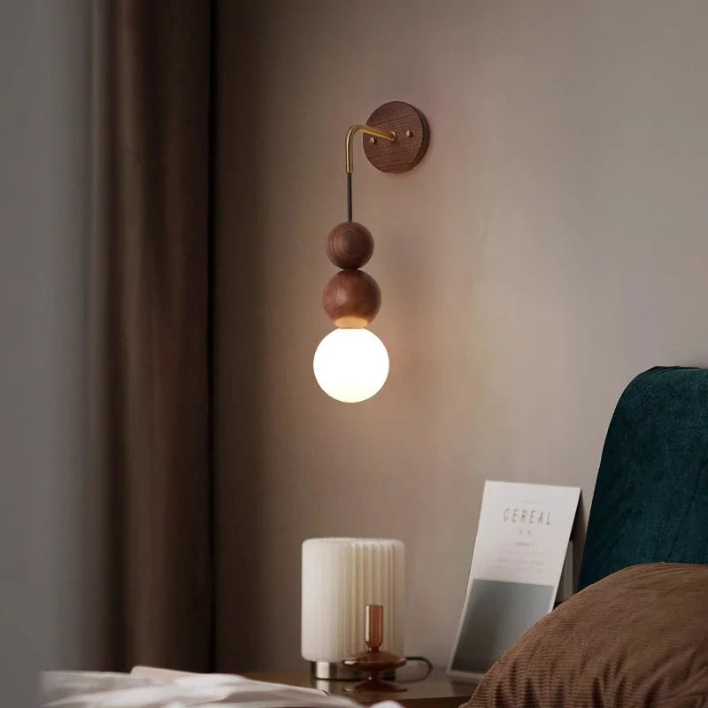 Elegant walnut wood wall lamp by LUXELY with brass arm and glowing globe, styled in a modern bedroom interior.