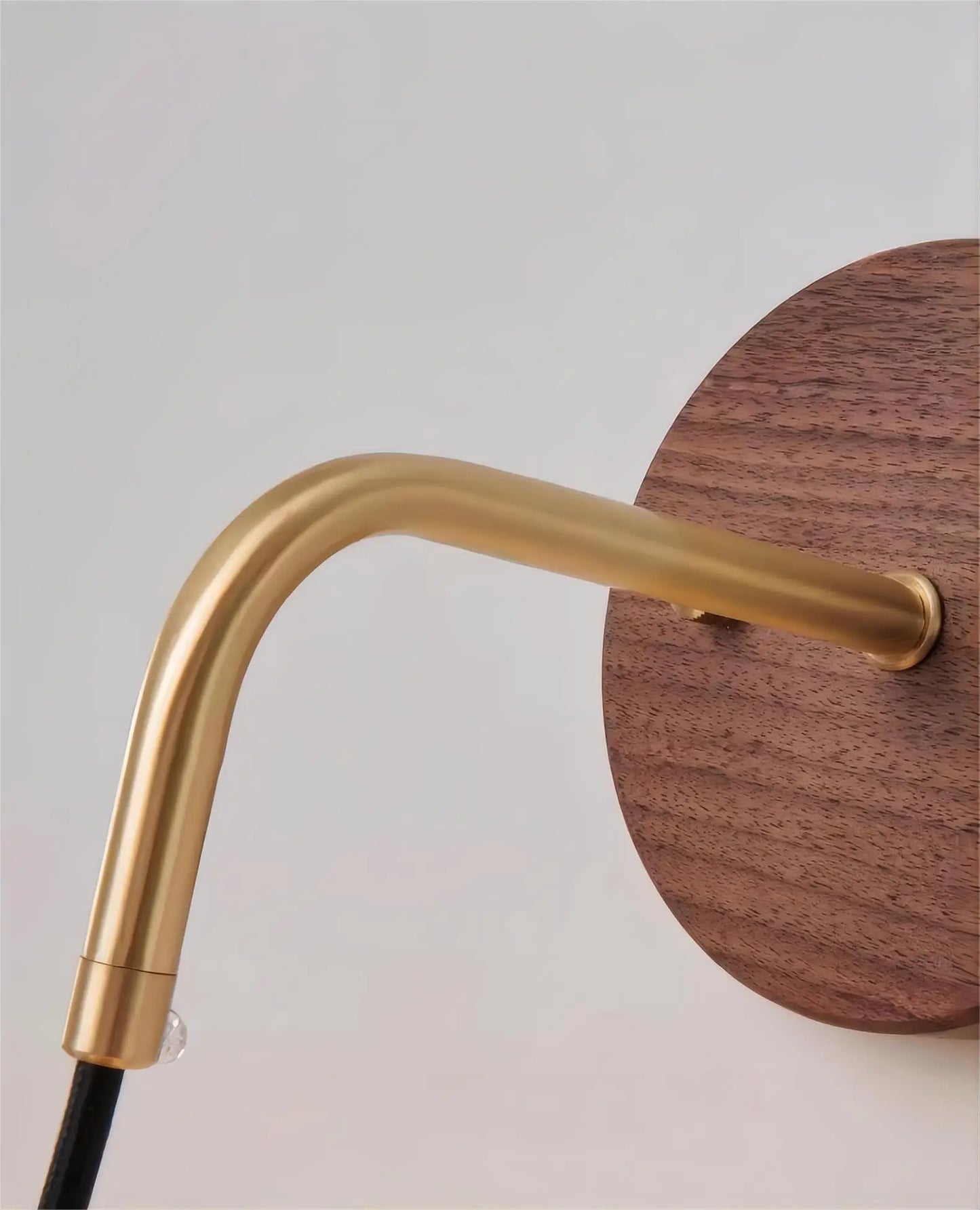 Detail of brass arm and walnut wood base on LUXELY wall light, showcasing premium materials and elegant design.