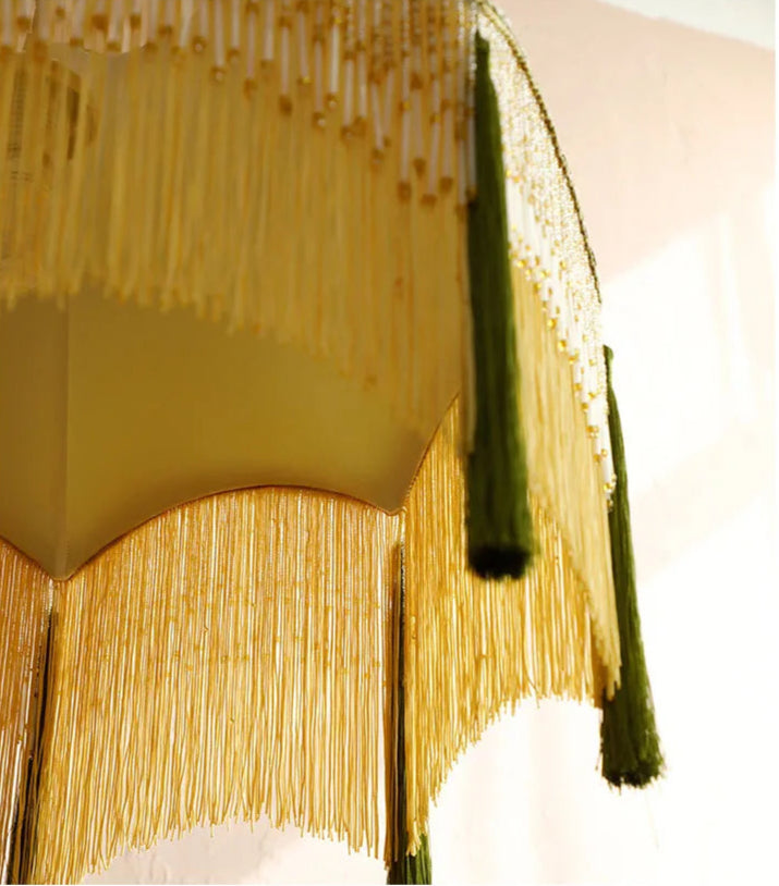Macro view of golden fringe and green tassels on velvet chandelier, emphasizing its luxurious vintage detailing.