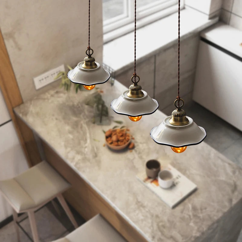 Set of three white ceramic pendant lights with brass fittings above a marble kitchen island, perfect for farmhouse kitchens.