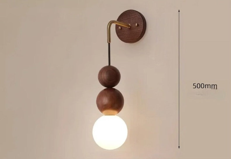 LUXELY walnut wood wall light with brass arm and 500mm height, featuring glowing glass globe for ambient lighting.