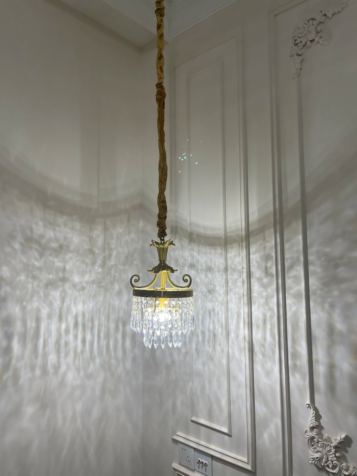 Copper crystal chandelier lit in a classic room, casting decorative light patterns on the wall for a cozy atmosphere.