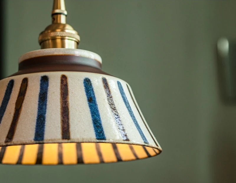 Close-up of striped ceramic pendant lamp with LED bulb and copper top, showcasing hand-painted vertical lines.