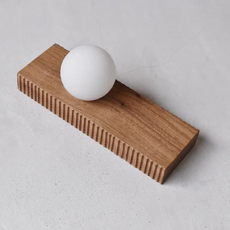 LUXELY walnut wall lamp placed on a flat surface, featuring a ribbed wood texture and spherical white light.