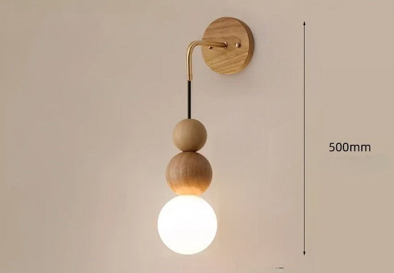 Light wood version of LUXELY wall sconce with brass accent and 500mm height, glowing glass globe for soft room lighting.