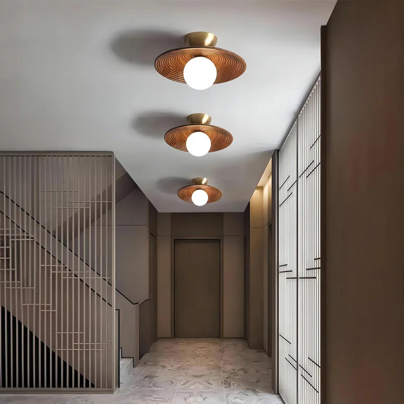 Set of three wood flush mount ceiling lights with brass accents illuminating a hallway, perfect for modern and wabi-sabi inspired spaces.