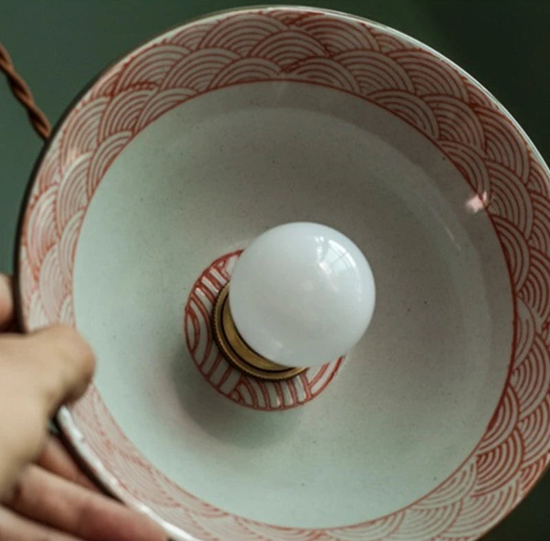 Close-up of orange wave-patterned ceramic pendant lamp with LED bulb, casting warm ambient light.