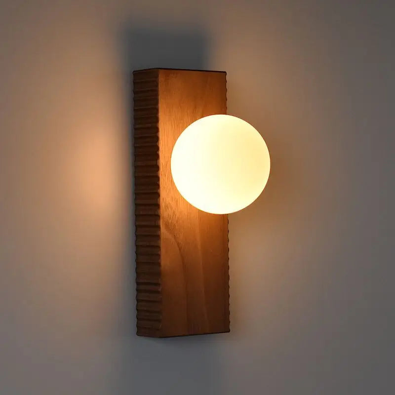 LUXELY walnut wood wall lamp illuminated on a wall, showcasing warm ambient bedroom lighting with a modern design.