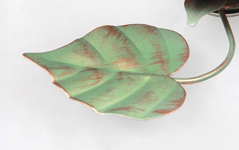 Close-up of green leaf detail on French rose chandelier. Handcrafted metal leaf complements romantic pink floral design.