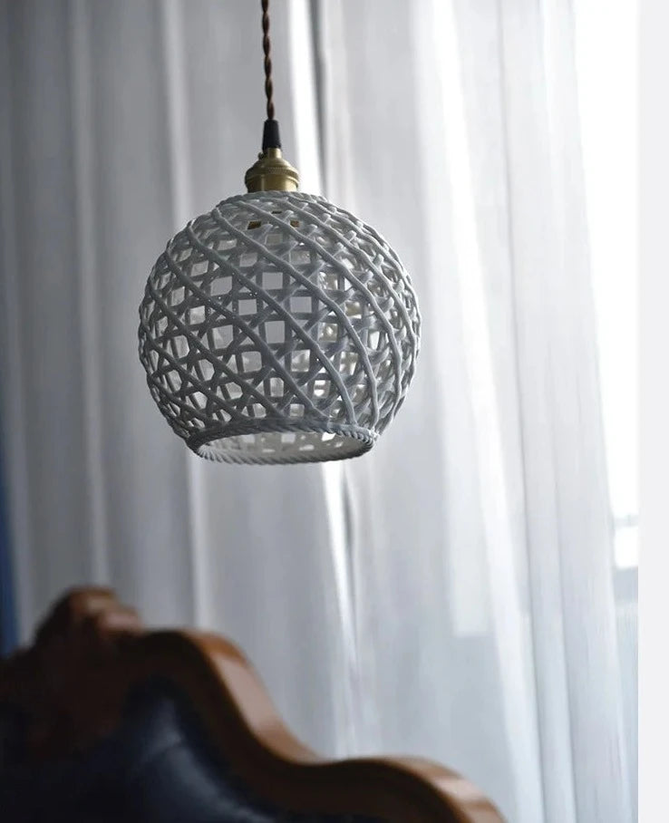 White spherical ceramic pendant light by LUXELY hanging near a window, ideal for soft ambient lighting in living spaces.