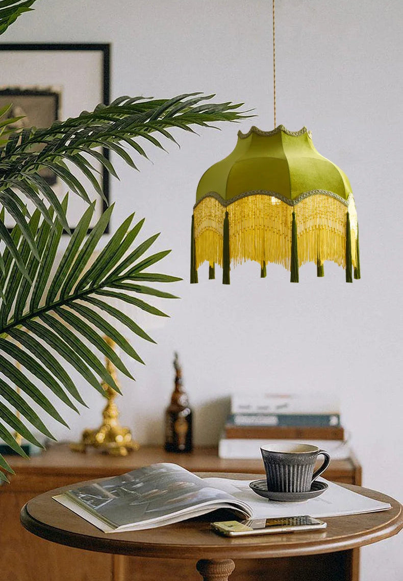 Elegant green velvet chandelier with yellow fringe above a wooden table, enhancing cozy reading nook ambiance.