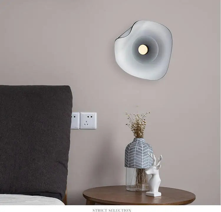 Modern glass wall lamp with soft glow mounted in a bedroom, blending art deco style with minimalist interior design.