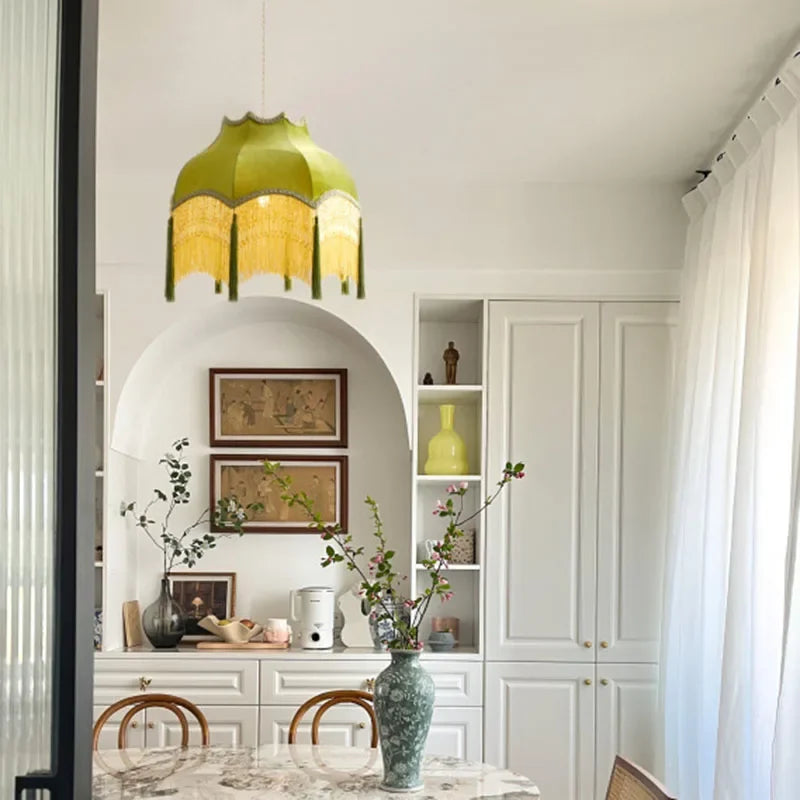 Green velvet tassel chandelier hanging in a white dining room, offering a luxurious focal point for classic interiors.
