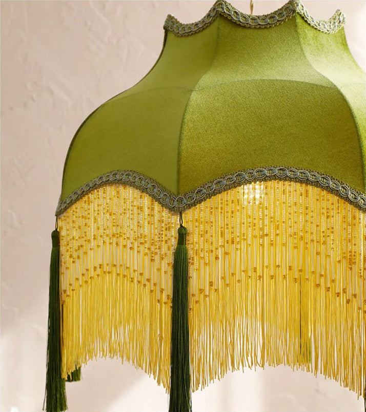 Close-up of green velvet chandelier with intricate gold fringe and tassels, highlighting its vintage craftsmanship.