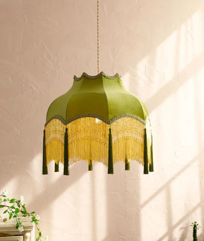 French velvet chandelier in green with gold tassels, casting warm light on a textured wall for vintage elegance.
